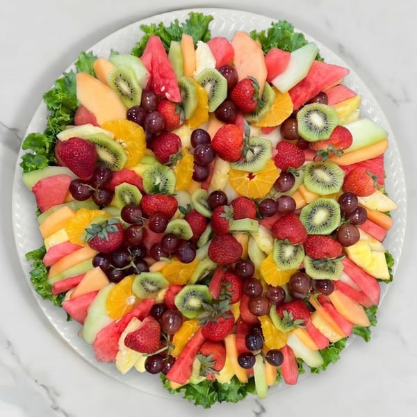 A vibrant fruit platter with strawberries, kiwi, grapes, watermelon, cantaloupe, and oranges on lettuce.