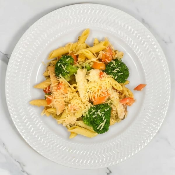 Penne pasta with chicken, broccoli, carrots, and shredded cheese on a white plate.