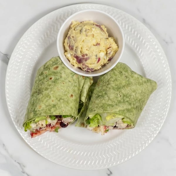 Two green wraps filled with chicken salad, lettuce, and cranberries, with a side of potato salad.